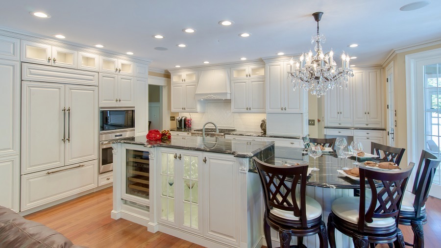 An ornate white kitchen with an island, glass cabinets and wine storage.