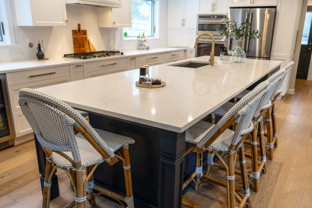 A large kitchen island with a white countertop and navy blue cabinets. Wood and gold accents elevate this island to something extraordinary. 